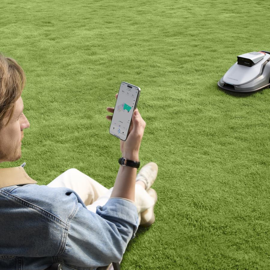 Mann steuert den TerraMow Mähroboter entspannt per App vom Rasen aus